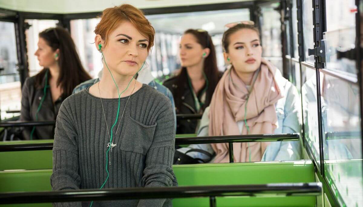 Slika dekleta v vlakcu Urbanu, ki med vožnjo preko slušalk posluša opis znamenitosti Ljubljane